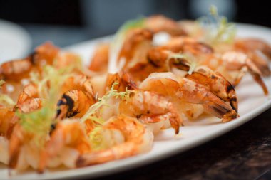 Beyaz bir tabakta garnitürle servis edilen ızgara karides aperatifinin yakın çekimi. Yemek promosyonları, restoran menüleri ve mutfak sunumları için ideal. Gurme yemek için yüksek kaliteli görüntü