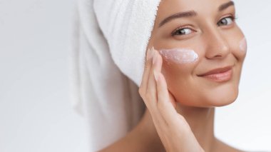 Beyaz tenli beyaz bir kadın yanaklarına nemlendirici krem sürüyor. Kaliteli cilt bakımı ve sağlık fotoğrafı güzellik, spa, kozmetik veya yaşam tarzı tanıtımı için idealdir..
