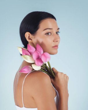 Pembe bir nilüfer çiçeği buketi tutan genç bir kadının zarif yan profili. Dinginlik ve güzellik saçıyor. Minimalist arka plan ve yumuşak ışıklandırma huzurlu ve huzurlu bir atmosfer yaratır.