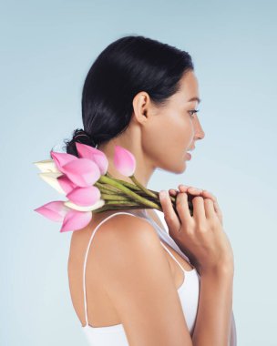 Yan profildeki zarif kadın omzunda doğal güzellik ve cilt bakımını temsil eden pembe nilüfer tomurcukları tutuyor. Spa tedavileri, güzellik ürünü reklamları ve lüks için mükemmel.