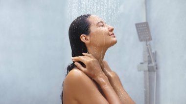 Islak saçlı sakin bir kadın, gözleri kapalı rahatlatıcı bir duş alır, rahatlama ve kendine bakmanın vücut bulmuş halidir. Sağlık, güzellik ve cilt bakımını spa ya da kişisel bakım reklamlarında desteklemek için mükemmel..