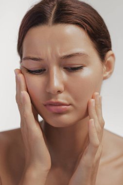 Kafkasyalı, gözleri kapalı bir kadın yanaklarını görünür bir rahatsızlıkla bastırıyor. Yüz veya diş ağrısı olduğunu söylüyor. Cilt hassasiyeti, stres ya da tıbbi kaynaklı görsel yayınlar için ideal.