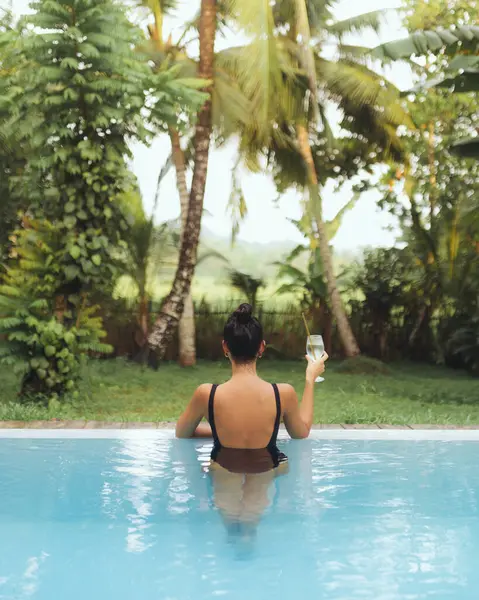 Beyaz bir kadın, yemyeşil yemyeşil bir havuzda içki içiyor. Lüks seyahatler, tatiller, rahatlama, tatil beldesi, tropikal kaçamak ve kişisel bakım kampanyaları için ideal..