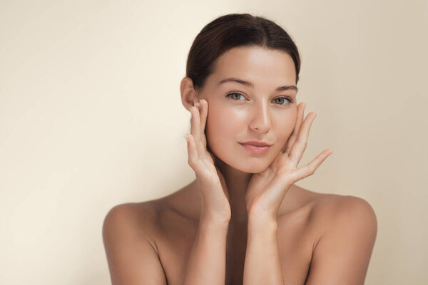 A young woman with flawless, radiant skin gently touching her face and posing confidently. Perfect for skincare, beauty, wellness, and cosmetic product advertisements. 