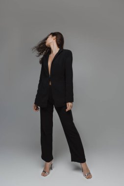 Siyah takım elbiseli, gömleksiz, kendine güvenen bir pozda saçlarını savuran zarif bir genç kadın. Moda yazıları, minimalist reklamlar ve lüks yaşam tarzı kavramları için mükemmel.. 