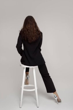 Siyah takım elbiseli, gümüş topuklu sandalyede sırtı dönük oturan şık genç bir kadın. Moda yazıları, modern zarafet ve minimalist kavramlar için mükemmel.. 