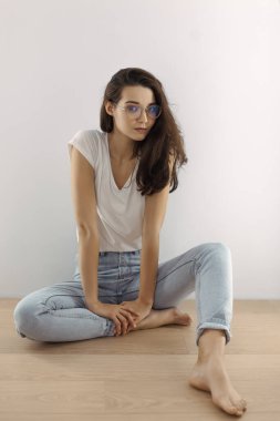 Kendine güveni tam, gözlüklü ve rahat bir şekilde yerde oturan rahat bir kadın. Yaşam tarzı kavramları, moda kampanyaları ve modern tarz markalaşması için mükemmel.. 