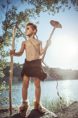 Caveman, taş baltalı erkeksi adam ve nehir kenarında yay avı. Tarih öncesi kabile çocuğu doğada açık havada. Genç tüylü ve kirli vahşi, savaşçı ve avcı. Hayvan derisinde ilkel buz devri adamı