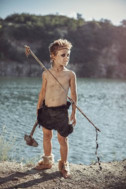 Caveman, taş baltalı erkeksi adam ve nehir kenarında yay avı. Tarih öncesi kabile çocuğu doğada açık havada. Genç tüylü ve kirli vahşi, savaşçı ve avcı. Hayvan derisinde ilkel buz devri adamı