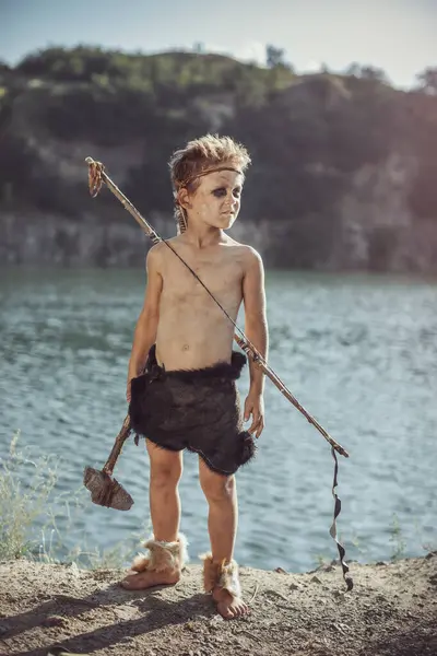 Caveman, taş baltalı erkeksi adam ve nehir kenarında yay avı. Tarih öncesi kabile çocuğu doğada açık havada. Genç tüylü ve kirli vahşi, savaşçı ve avcı. Hayvan derisinde ilkel buz devri adamı