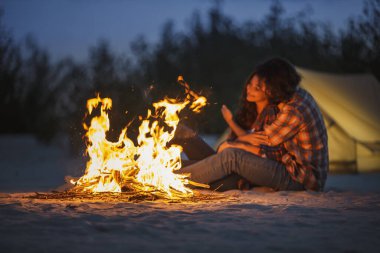 Huzurlu bir kamp gezisi sırasında parlayan bir kamp ateşinin yanında oturan sevgi dolu çift. Sıcak alevler açık hava ortamını aydınlatıyor, romantizm, seyahat ve yaşam tarzı kavramları için mükemmel.. 
