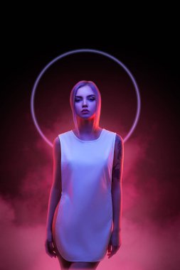 Sarışın kadın fütüristik halo efektli neon ışıklarda poz veriyor, siber punk estetiğini çağrıştırıyor. Bu yüksek kaliteli görüntü modern stil, teknoloji ve güzel sanatları harmanlıyor, kavramsal ve kavramsal için mükemmel.