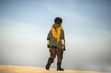 Kıyamet sonrası donanımlı genç bir çocuk elinde silahla çöl ufkuna doğru yürüyor. Sinema, fantezi tanıtımı ve temalı macera içeriği için yüksek kaliteli bilim kurgu hayatta kalma konsepti.