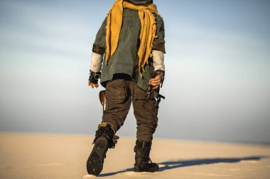 Kafkasyalı çocuk elinde tabancayla çölde kıyamet sonrası kıyafetleriyle tek başına yürüyor. Yüksek kaliteli bilim kurgu teması, film afişleri, hikaye anlatma ve hayatta kalma konsepti sanatı için ideal..