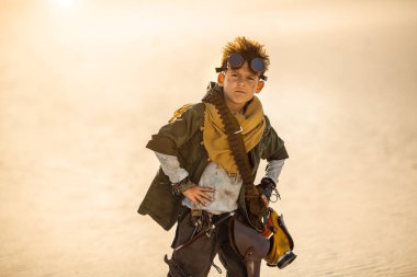 Elinde şişe tutarken gözlük, eşarp ve taktik kıyafet takan, kıyamet sonrası savaşçısı olarak tasvir edilmiş yüksek kaliteli bir çocuğun fantezi fotoğrafı. Dystopian, cosplay veya film teması için ideal.