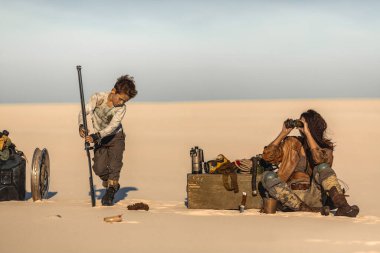 Apokaliptik kadın ve çocuk kampta dinleniyor. Arka planda ölü bir arazi var. Eski püskü giysiler içinde çekici bir savaşçı kız ve dövüşe hazırlanan kılıçlı acımasız bir çocuk. A