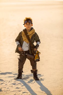 Kıyamet sonrası cyberpunk çocuk açık havada. Kıyamet sonrası nükleer zaman. Kıyamet günü kavramından sonraki hayat. Kendine güvenen bir poz, çöl ve ölü çorak duran eski züppon giysiler içinde genç bir adam savaşçı