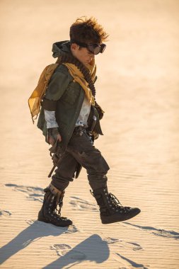 Kıyamet sonrası kostümü giymiş genç bir çocuk kumlu çölde tek başına yürüyor. Temalı posterler, sinematik tanıtım ve dramatik öykü içeriği için yüksek kaliteli bilim kurgu hayatta kalma kavramı.