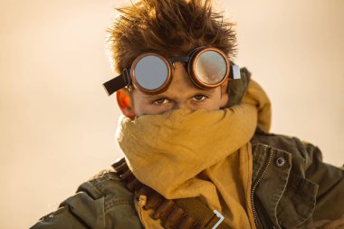 Kıyametten sonra hayatta kalan gözlük, eşarp ve sıcak çöl ışığında engebeli kıyafetler giyen genç bir çocuğun yüksek kalite kavramsal portresi. Disstopian veya fantezi görseller için ideal.