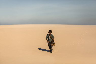 Kıyametten sonra çölün ortasında bir çocuk. Nükleer kıyametten sonraki insanlar. Kıyamet sonrası yaşam konsepti. Çöl ve ölü çorak arazi kopyalama alanı. Bıçaklı, gaz maskeli genç bir adam