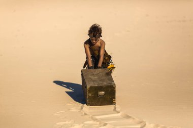 Kıyametten sonra çölün ortasında bir çocuk. Nükleer kıyamet sonrası patlaması. Kıyamet sonrası yaşam konsepti. Arka planda çöl ve ölü çöl var. Bıçaklı, gaz maskeli genç bir adam, göğsünü sürükleyen bir kupa.