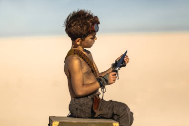 Kıyamet sonrası giysileri içinde gömleksiz bir çocuk çölde göğsünde otururken bıçağı inceliyor. Sinema, fantezi tanıtımları ve aksiyon görselleri için yüksek kaliteli bilim kurgu imajı ideal..