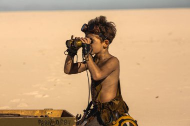 Kıyamet sonrası donanımlı tişörtsüz çocuk açık bir askeri sandığın yakınındaki çölü taramak için dürbün kullanıyor. Yüksek kaliteli bilim kurgu hayatta kalma konsepti sinematik hikaye anlatımı ve fantezi promosyonları için idealdir..