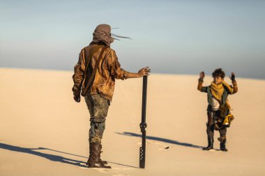 Çölde eli silahlı bir kadının önünde duran çocuk teslim olmayı öneriyor. Yüksek kaliteli bilim kurgu hayatta kalma görüntüsü sinematik drama, fantezi öyküleri ve çatışma tanıtımları için mükemmel..