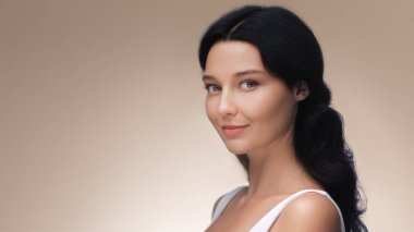 Parlak tenli ve doğal makyajlı beyaz bir kadının zarif stüdyo portresi, usulca gülümsüyor. Moda, cilt bakımı ve güzellik ürünü promosyon içeriği için ideal.