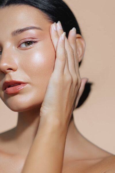 Крупный план латиноамериканки с сияющей, безупречной кожей и мягким натуральным макияжем, нежно касающейся ее лица. Идеально подходит для красоты, кожи, анти-старения или пластической хирургии рекламных материалов. 