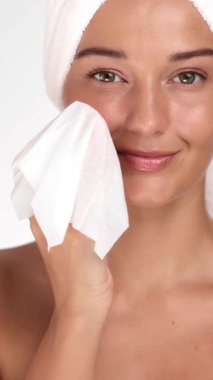 Kafasında havlu olan mutlu genç kadın makyajı yumuşak peçeteyle kaldırıyor. Güzellik, cilt bakımı, makyaj temizliği, yüz bakımı ve temiz yaşam tarzı içeriğinde kişisel bakım için ideal..