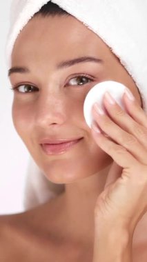 Beyaz havluyla yüzünü pamukla temizlerken gülümseyen beyaz bir kadın. Cilt bakımı, kozmetik alışkanlıkları, güzellik ürünleri ve sağlıklı yaşam tarzı tanıtımı kavramları.