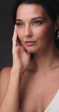 Stüdyoda yüzüne nazikçe dokunan beyaz bir kadının yavaş çekim görüntüleri. Kavramsal güzellik ve cilt tanıtımı. Parlak ciltli ve modaya uygun altın makyajlı..