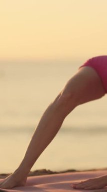 Pembe spor giysili güçlü, fit kadın altın saatinde deniz kenarında yoga pozu veriyor. Sağlık, zindelik ve vücut pozitifliği kampanyaları için yüksek kaliteli kavramsal görüntüler.