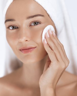 Nazik yüz temizleme için pamuk ped kullanan güzel beyaz bir kadın. Taze cilt bakımı ve kafasında havlu olan spa konsepti. Sağlık ve güzellik hizmetleri için ideal..