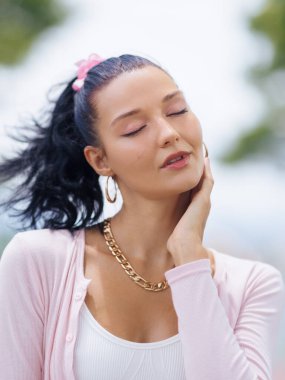 Sakin, genç, beyaz, gözleri kapalı ve makyajlı bir kadın yüzüne nazikçe dokunuyor. Cilt bakımı, güzellik, sağIık ve lüks tanıtım kampanyaları için doğal ışık idealiyle yakalanıyor..