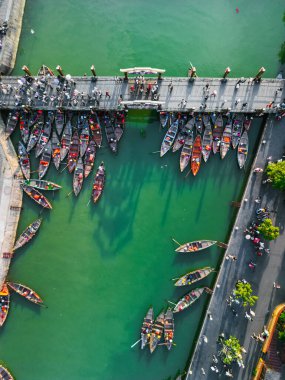 Hoi An, Vietnam 'daki bir yaya köprüsünün yakınına yanaşmış canlı ahşap teknelerin tepeden tırnağa fotoğrafı. Editör, seyahat, turizm ve kültürel stok fotoğrafı kullanımı için mükemmel..