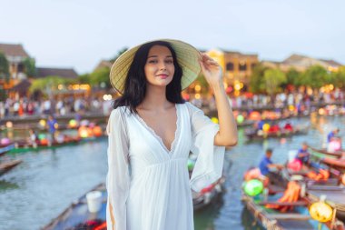 Akan beyaz elbiseli zarif genç bir kadın ve Vietnam, Hoi An 'da fener ışığında poz veren Vietnamlı non la hat. Seyahat reklamları, moda yazıları ve kültürel tanıtımlar için ideal..