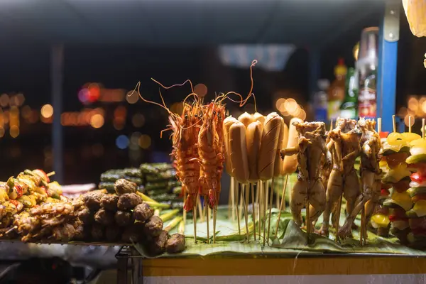 Hoi An 'daki gece pazarında leziz Vietnam sokak yemekleri. Sıcak ışıklar altında ızgara deniz ürünleri, sosisler ve etler sergileniyor. Mutfak ve seyahat promosyonları için harika..