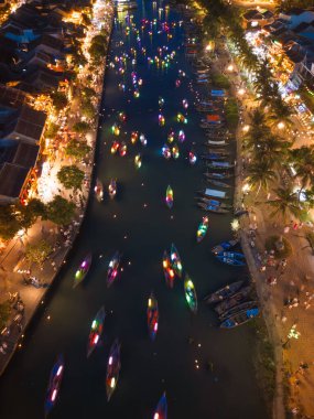 Hoi An 'ın nehrinin büyüleyici dikey görüntüsü. Geceleri renkli fener tekneleriyle dolu. Parlak ışıklar suyu yansıtırken, yerli halk ve turistler nehir kenarındaki şenlikli sokakların keyfini çıkarıyorlar..