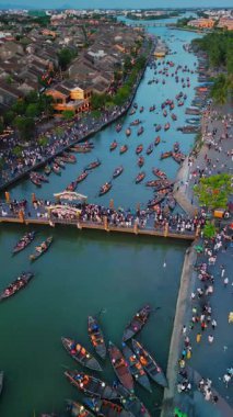 Hoi Nehri üzerindeki geleneksel ahşap teknelerin insansız hava aracı görüntüleri. Eski bir kasaba, Vietnam. Fenerler tekneleri aydınlatırken, kalabalık nehir kenarına dizildi. Seyahat, turizm ve kültür projeleri için ideal.