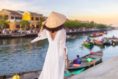 Hoi An, Vietnam 'da beyaz elbise ve konik şapka giyen zarif Asyalı kadının arka görünüşü fener teknelerine bakıyor - seyahat blogları, promosyonlar ve kültürel konsept görseller için ideal.