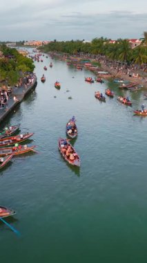 Hoi An, Vietnam 'da kalabalık bir köprünün üzerinde uçan bir insansız hava aracının hava videosu. Sonra nehir boyunca süzülerek kayıklar ve geleneksel evlerle dolu. Turizm, kültür ve tanıtım için mükemmel..