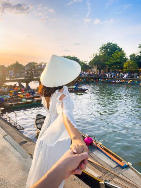 Beyaz elbiseli şık bir Asyalı kadın ve Vietnam 'da Hoi An nehrinin kenarında eşinin şapkasını tutuyor. Romantik seyahat konsepti yaşam tarzı, turizm ve yüksek kaliteli tanıtımlar için mükemmel..