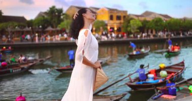 Beyaz saçlı, şapkalı, Hoi An, Vietnam 'da nehri esintisinin tadını çıkaran bir kadının ağır çekim görüntüleri. Yaşam tarzı, seyahat ve moda projelerinde kullanım için ideal.