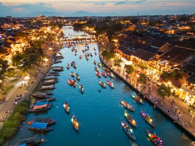 Hoi An, Vietnam 'da nehir boyunca süzülen fener ışıklı teknelerin akşam manzarası, parlayan caddeler ve canlı kalabalıklar - seyahat, kültür, editör ve yaşam tarzı görselleri için ideal.