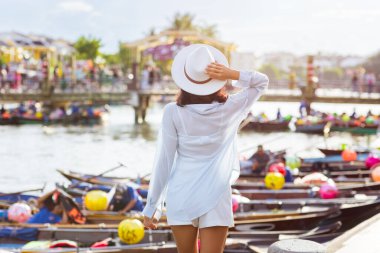 Beyaz gömlek giyen ve elinde şapka tutan genç bir kadın Hoi An kasabası, Vietnam 'da, renkli fener teknelerini seyrediyor. Yaşam tarzı, seyahat ve turizm promosyonları için mükemmel..
