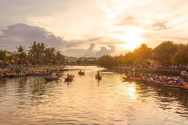 Vietnam 'ın Hoi An kentindeki Thu Bon Nehri' ndeki geleneksel teknelerin altın saat sahnesi. Palmiyelerin ve çatıların yumuşak yansımaları ve siluetleri huzurlu, rüya gibi bir yolculuk ve rahatlama ortamı yaratır..