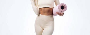 Stüdyoda, üzerinde pembe yoga minderi olan krem rengi spor giysili bir kadın bedeni görülüyor. Sağlık reklamları, fitness blogları, spa tanıtımları ya da yoga yaşam tarzı görselleri için harika..