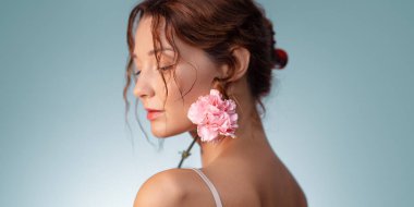 Yumuşak makyajlı, omuzunda pembe karanfil olan zarif, beyaz bir kadın. Kadınsı güzellik ve cilt bakımı sağlık, moda ve parfüm reklamları için idealdir..